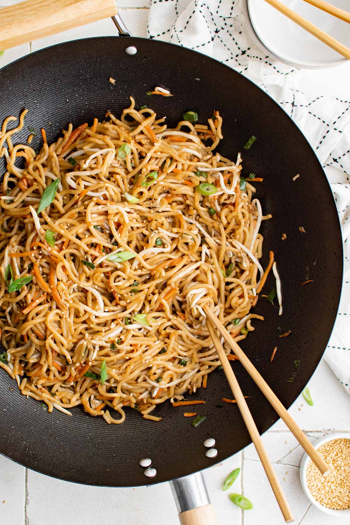 A wok with noodles, veggies and chopsticks.