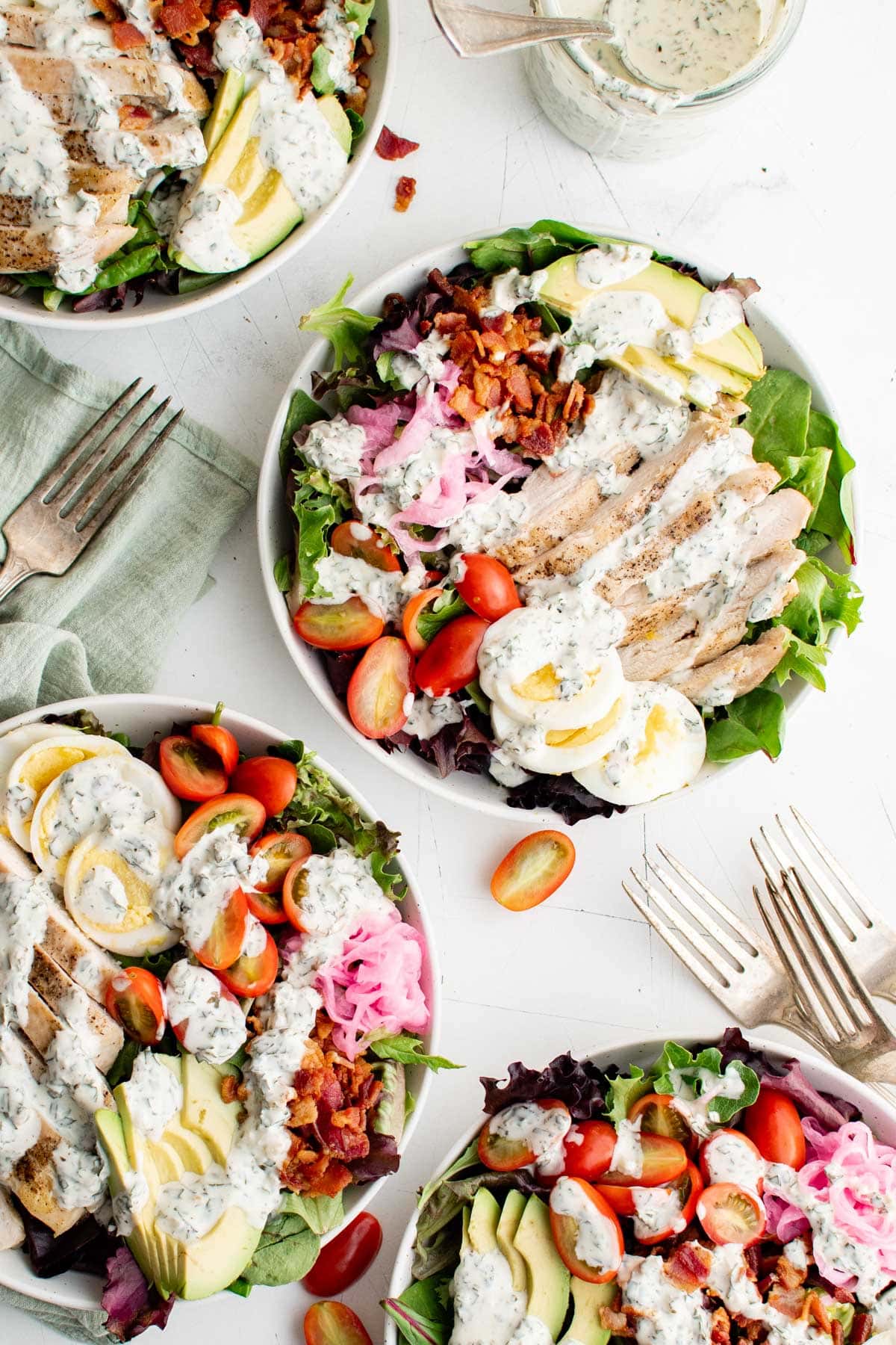 Several cobb salads in white bowls with forks.