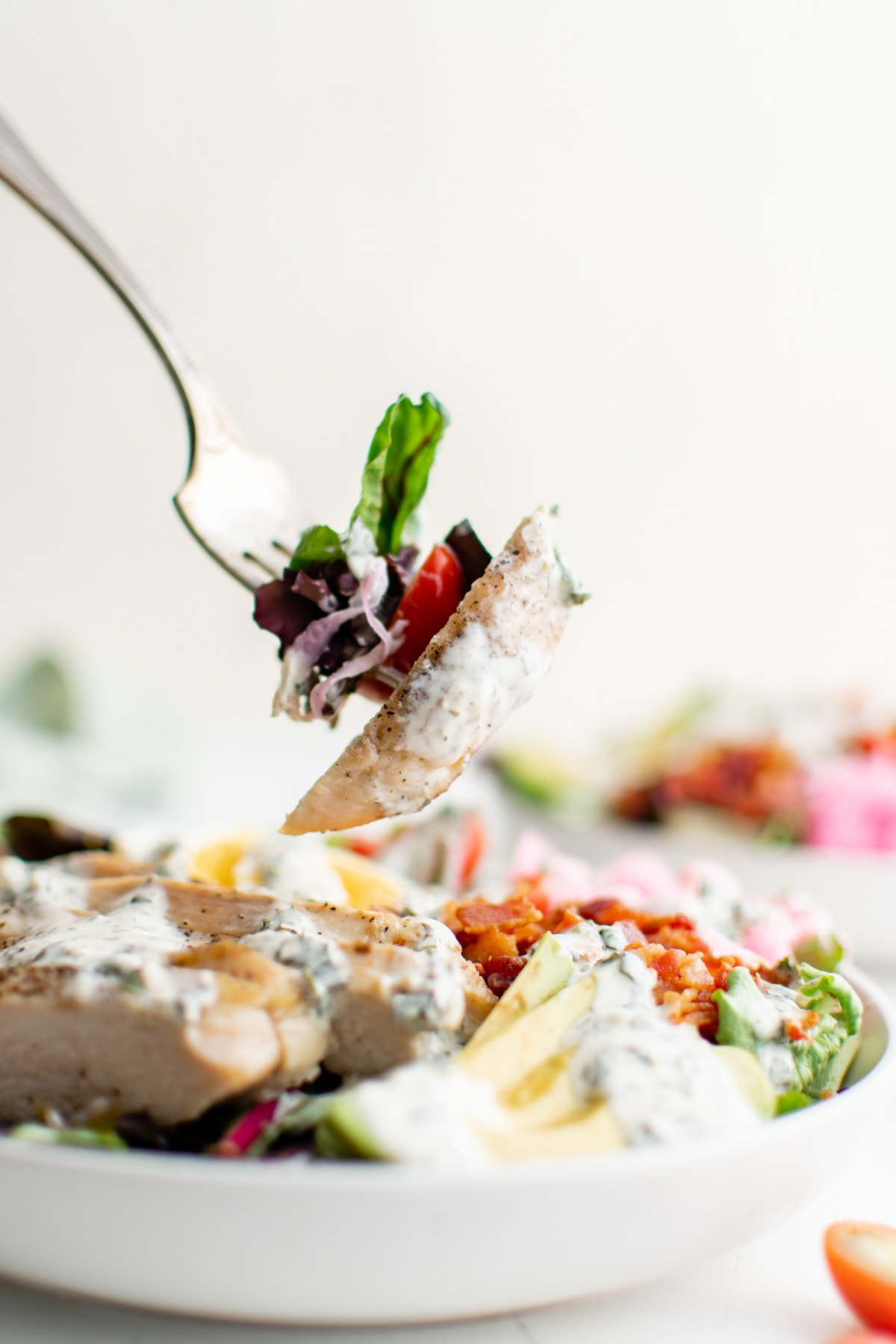 A fork taking some of the cobb salad out of the bowl.