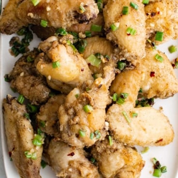 Baked chicken wings on w white platter with a green kitchen towel and sliced green onions.