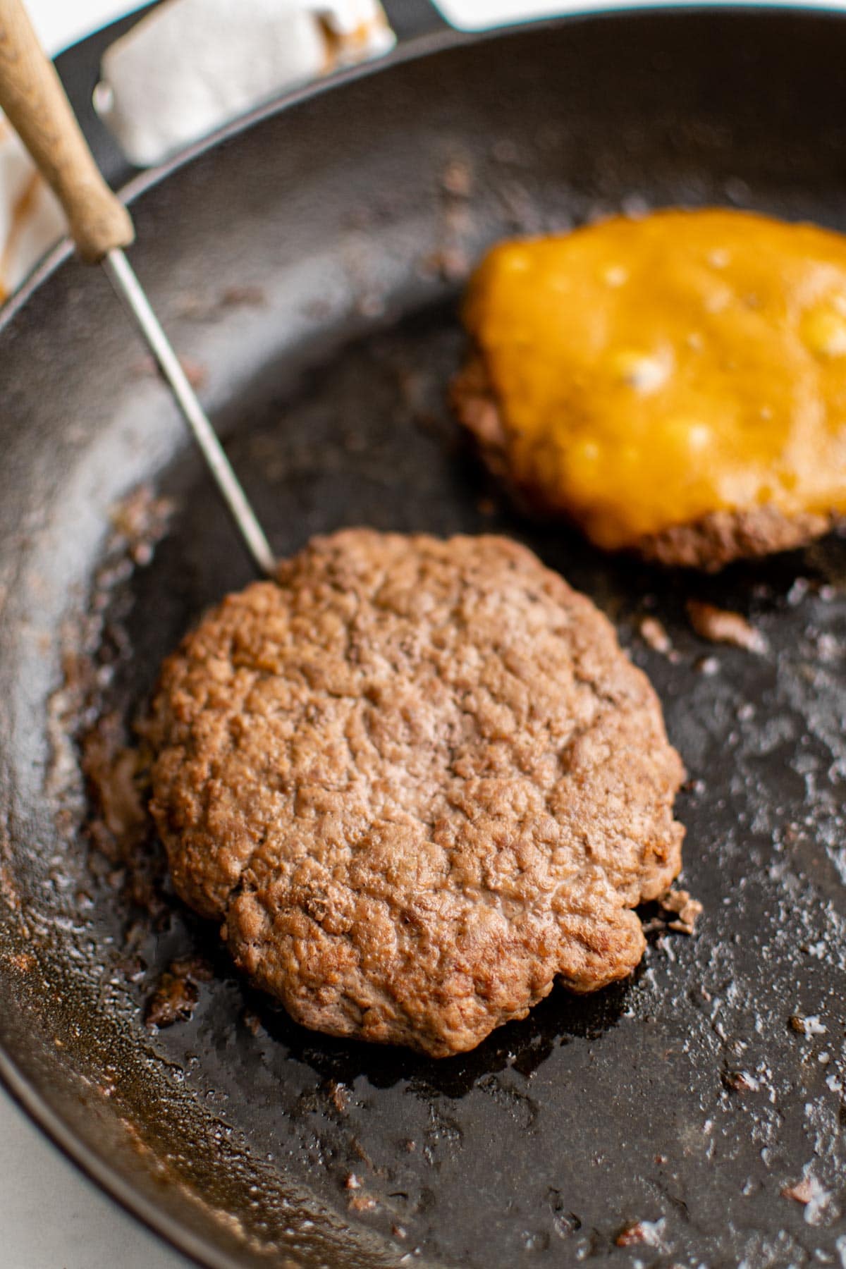A well done hamburger patty in a skillet, held up by a metal spatula. 