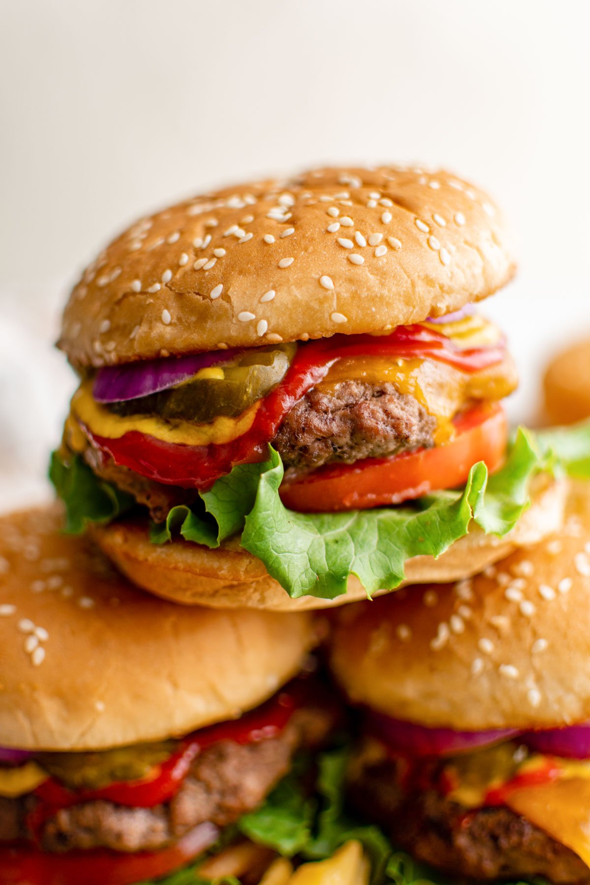 stack of 3 cheeseburgers with toppings. 