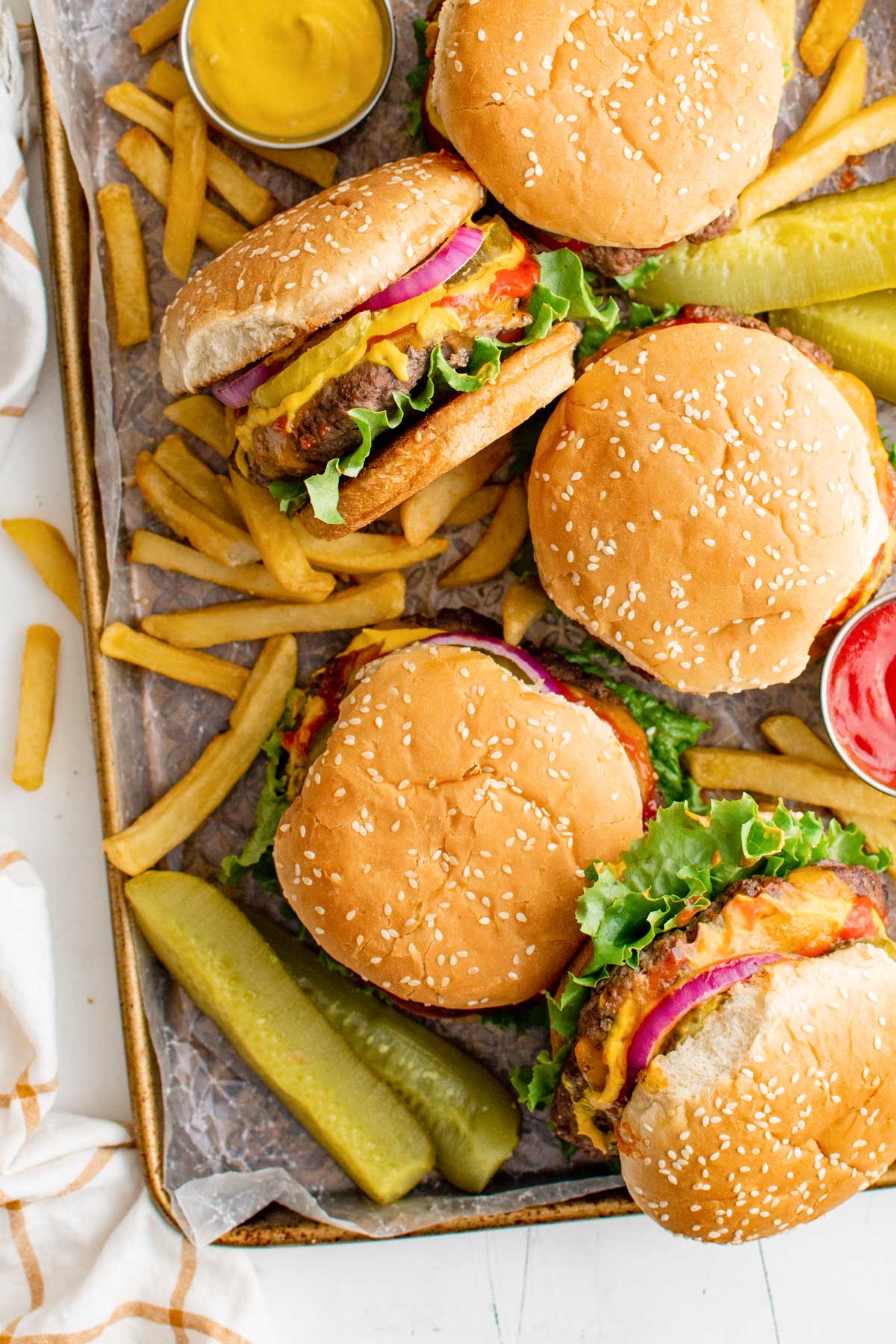 Metal baking sheet with cheeseburgers, fries and pickles.