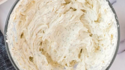 Soft cream cheese mixed with herbs in a glass bowl.
