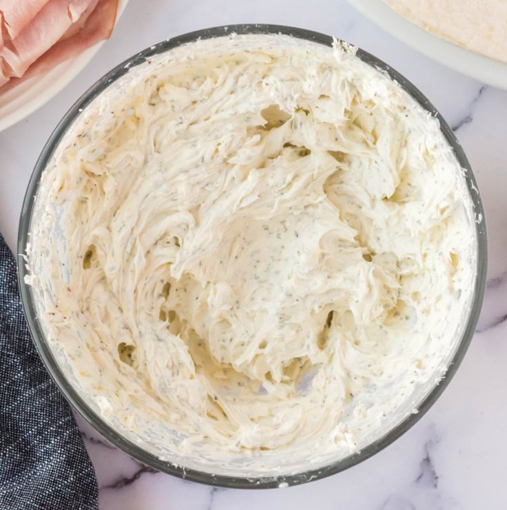 Soft cream cheese mixed with herbs in a glass bowl.