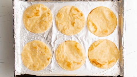 Baked tortillas on a foil lined baking sheet.