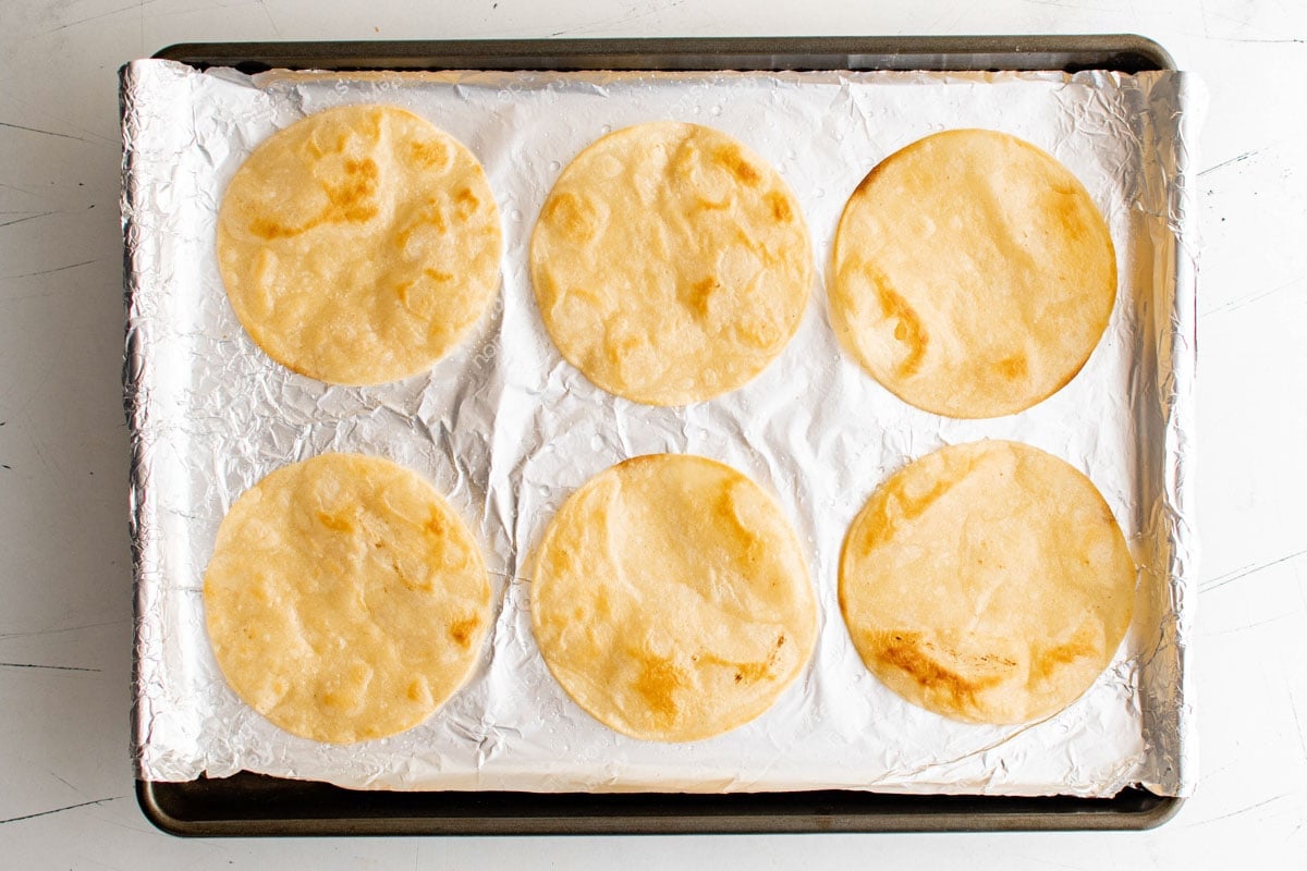 Baked tortillas on a foil lined baking sheet.