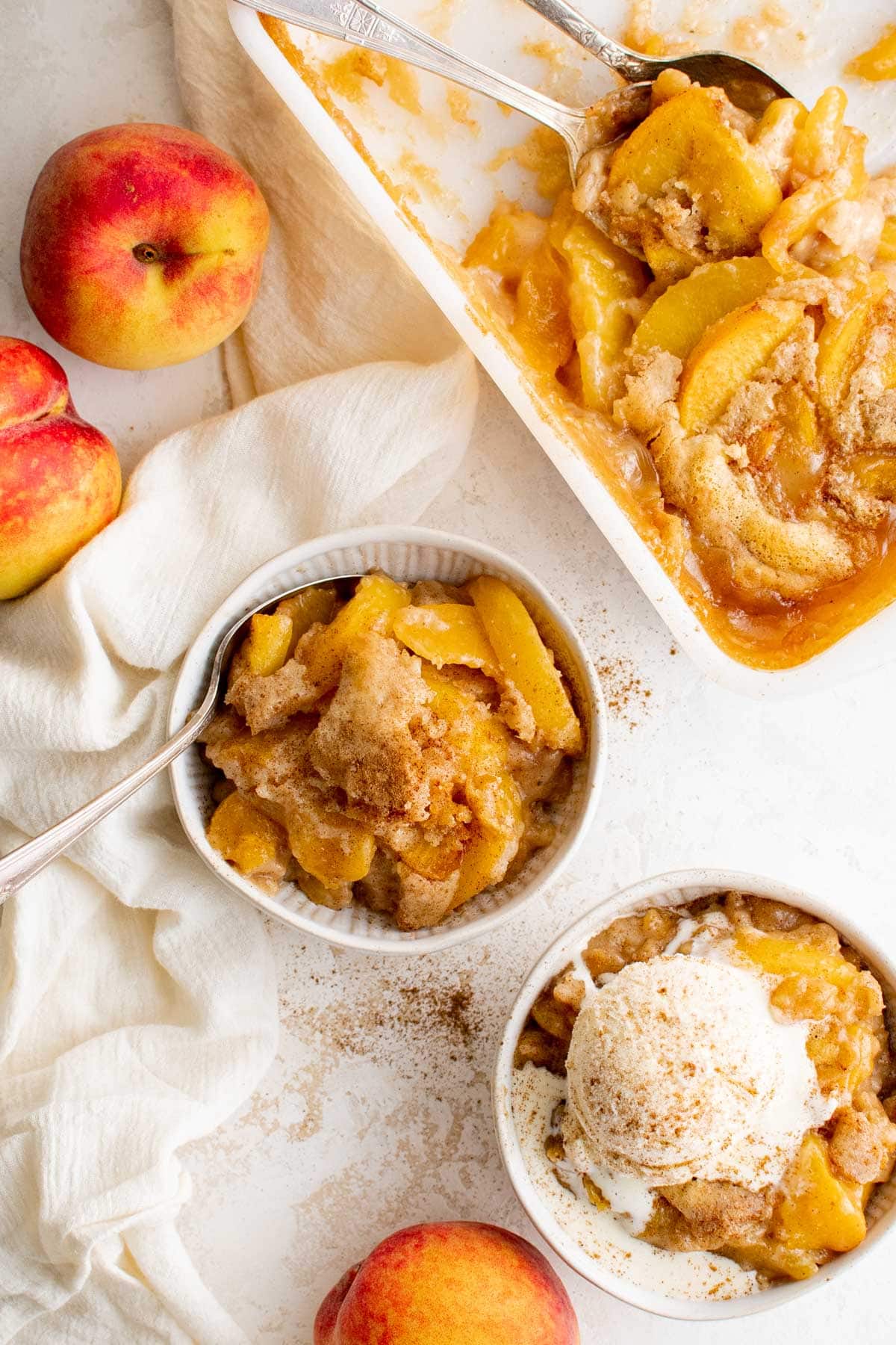 Small bowls with peach cobbler and vanilla ice cream, a pan with peach cobbler. 