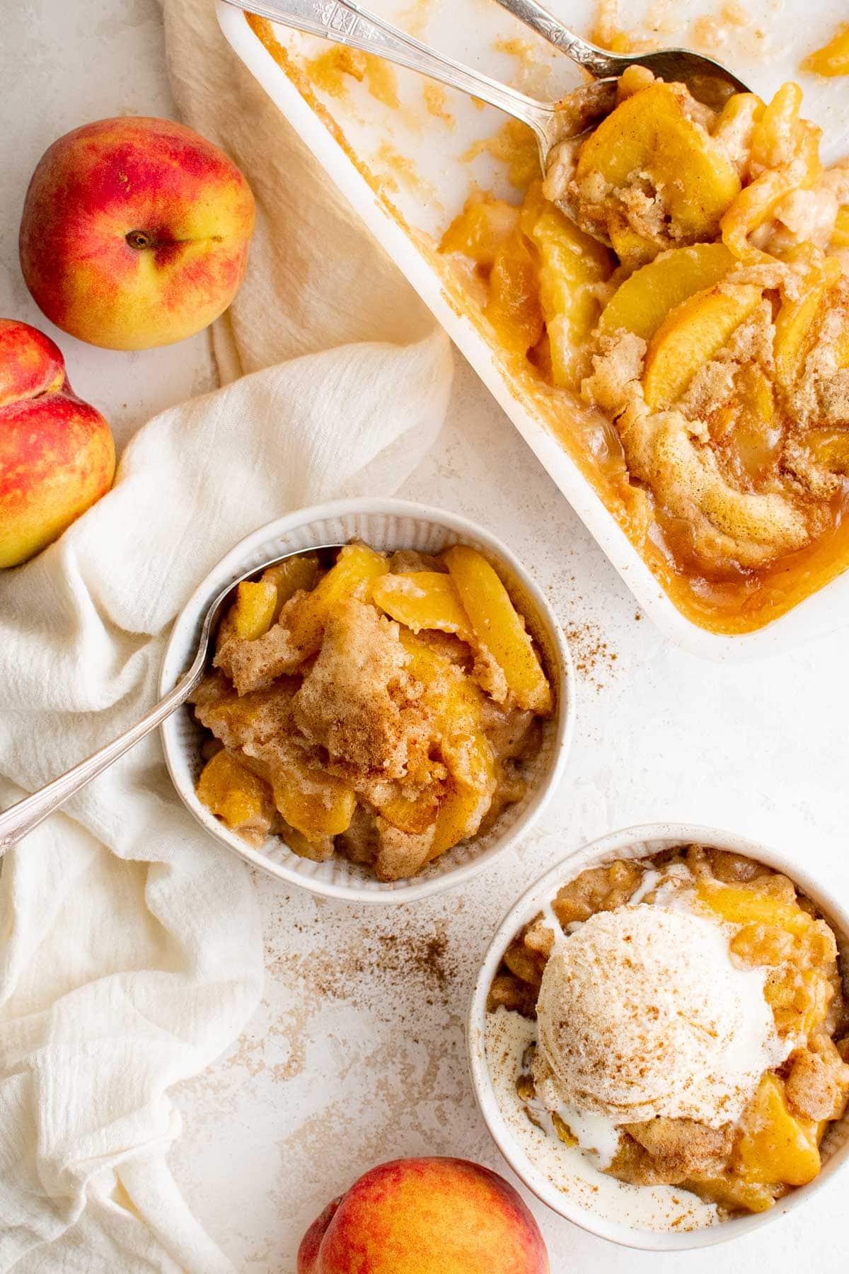 Small bowls with peach cobbler and vanilla ice cream, a pan with peach cobbler.