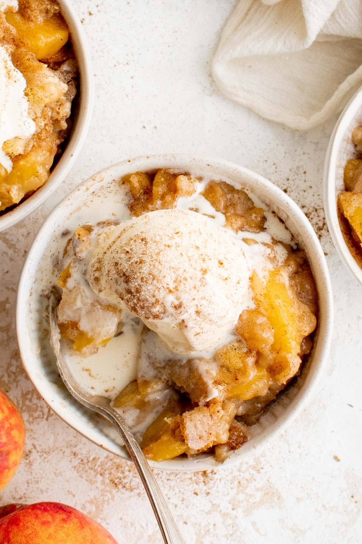 Bisquick Peach Cobbler in a white bowl with a scoop of vanilla ice cream.