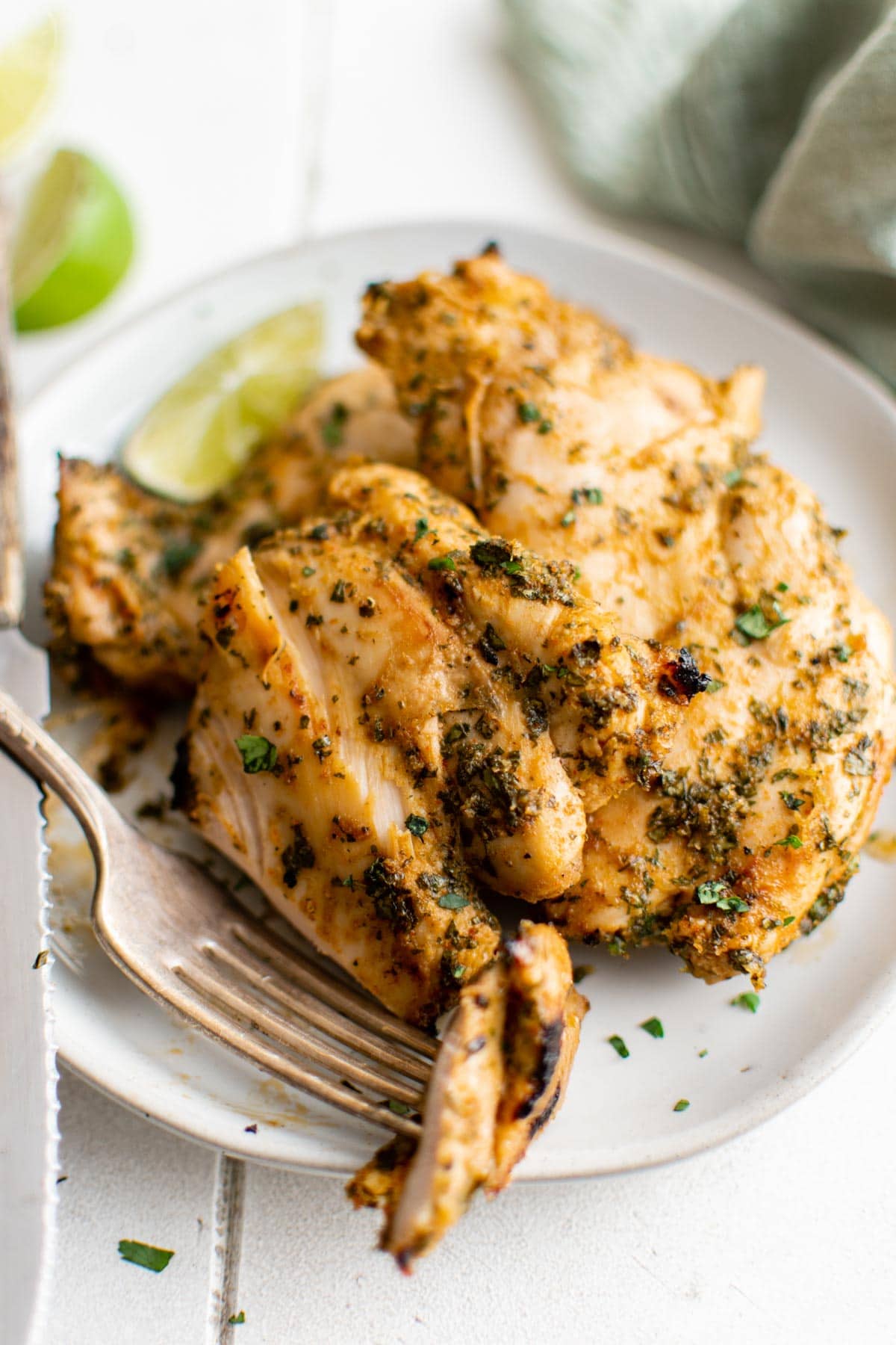 Chicken thighs with cilantro and lime marinade on a late, sliced, with a fork.