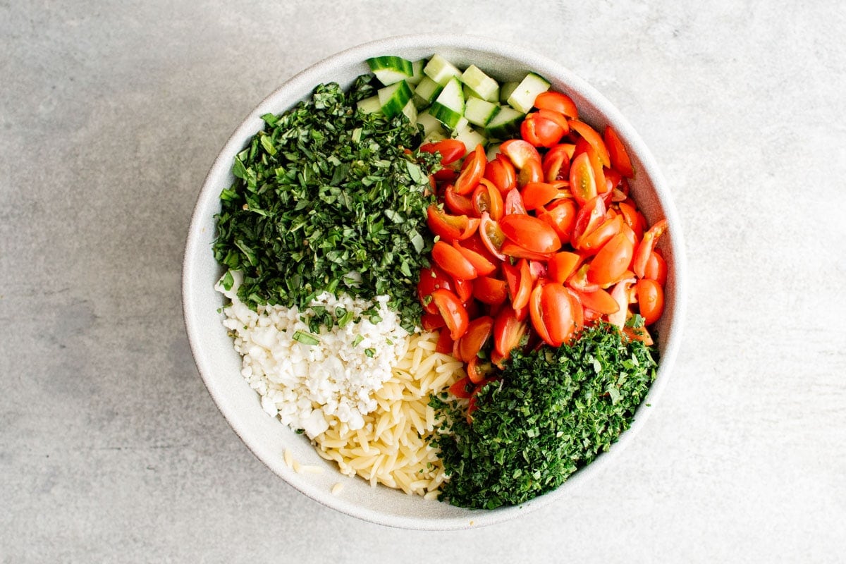 Ingredients for Orzo salad in a white bowl.