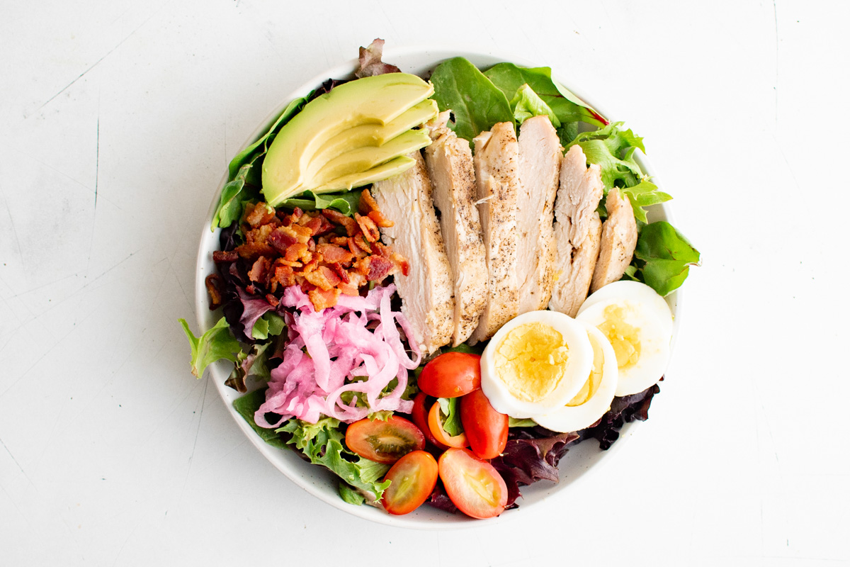 Salad in a bowl with eggs, avocado, pickled onions, bacon and chicken.