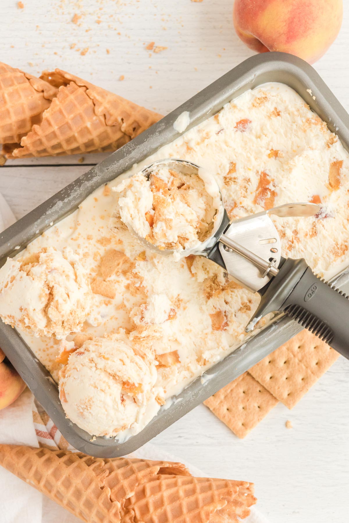 Loaf pan with homemade peach ice cream and an ice cream scoop.