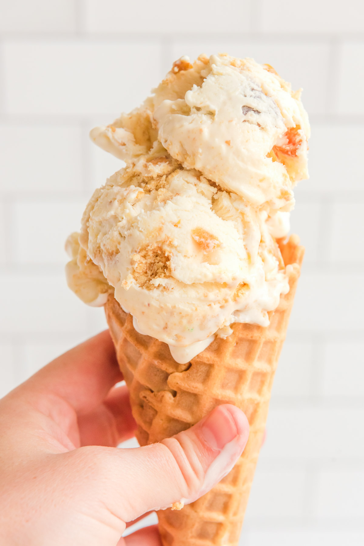 A hand holding a waffle cone with 2 scoops of peach ice cream. 