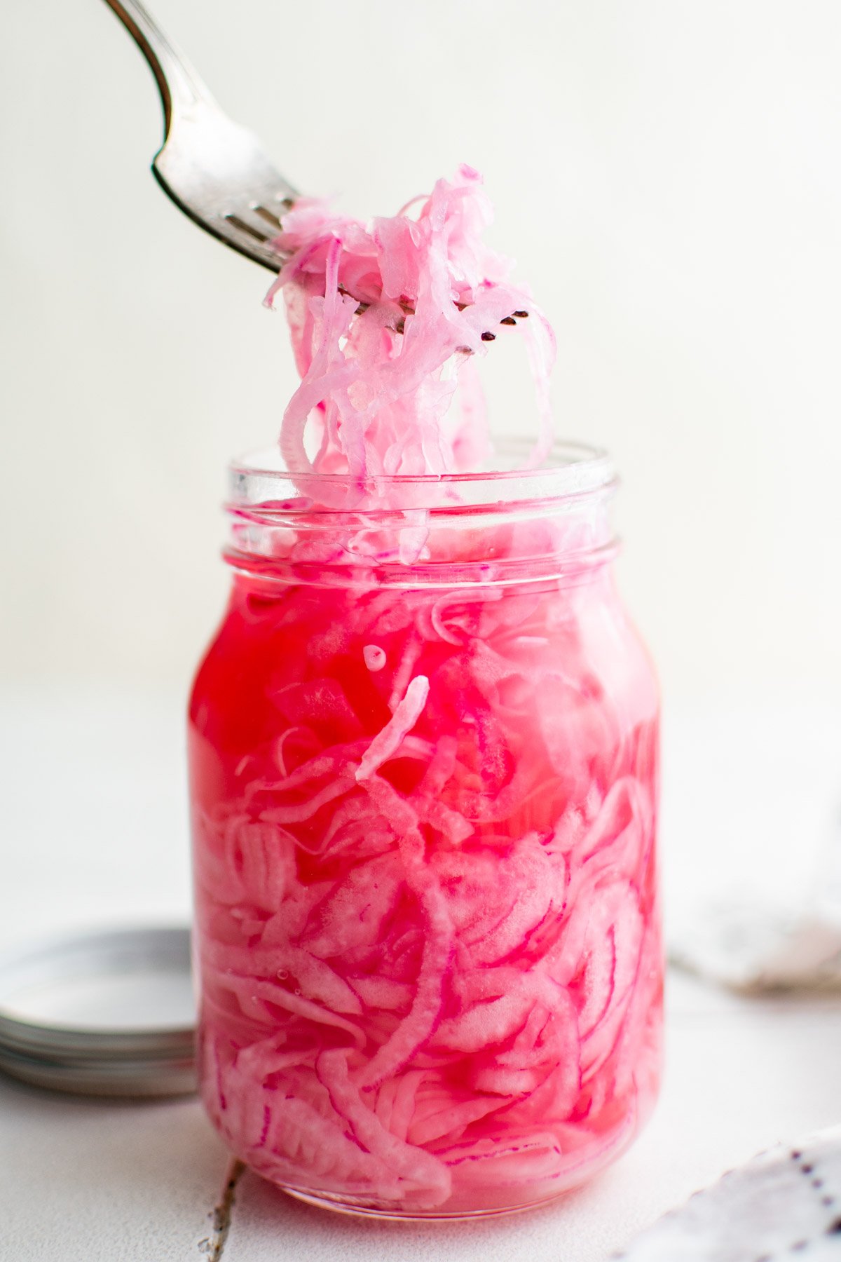 Pickled red onions in a jar with liquid and a fork.