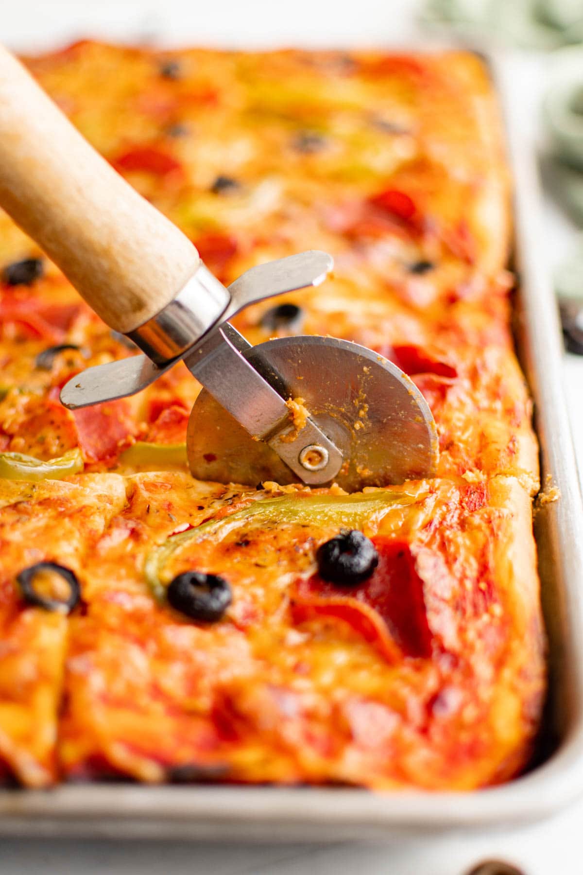 Sheet pan pizza being cut with a pizza cutter. 