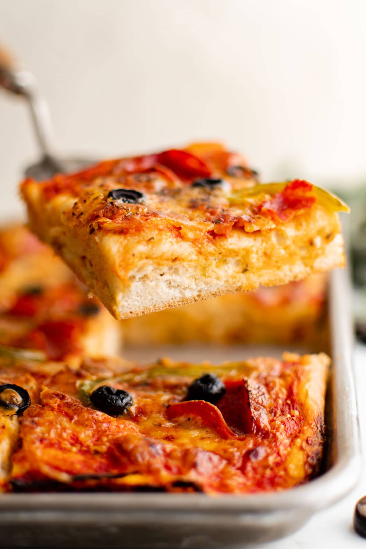 Sheet pan pizza, a slice being lifted by a spatula.