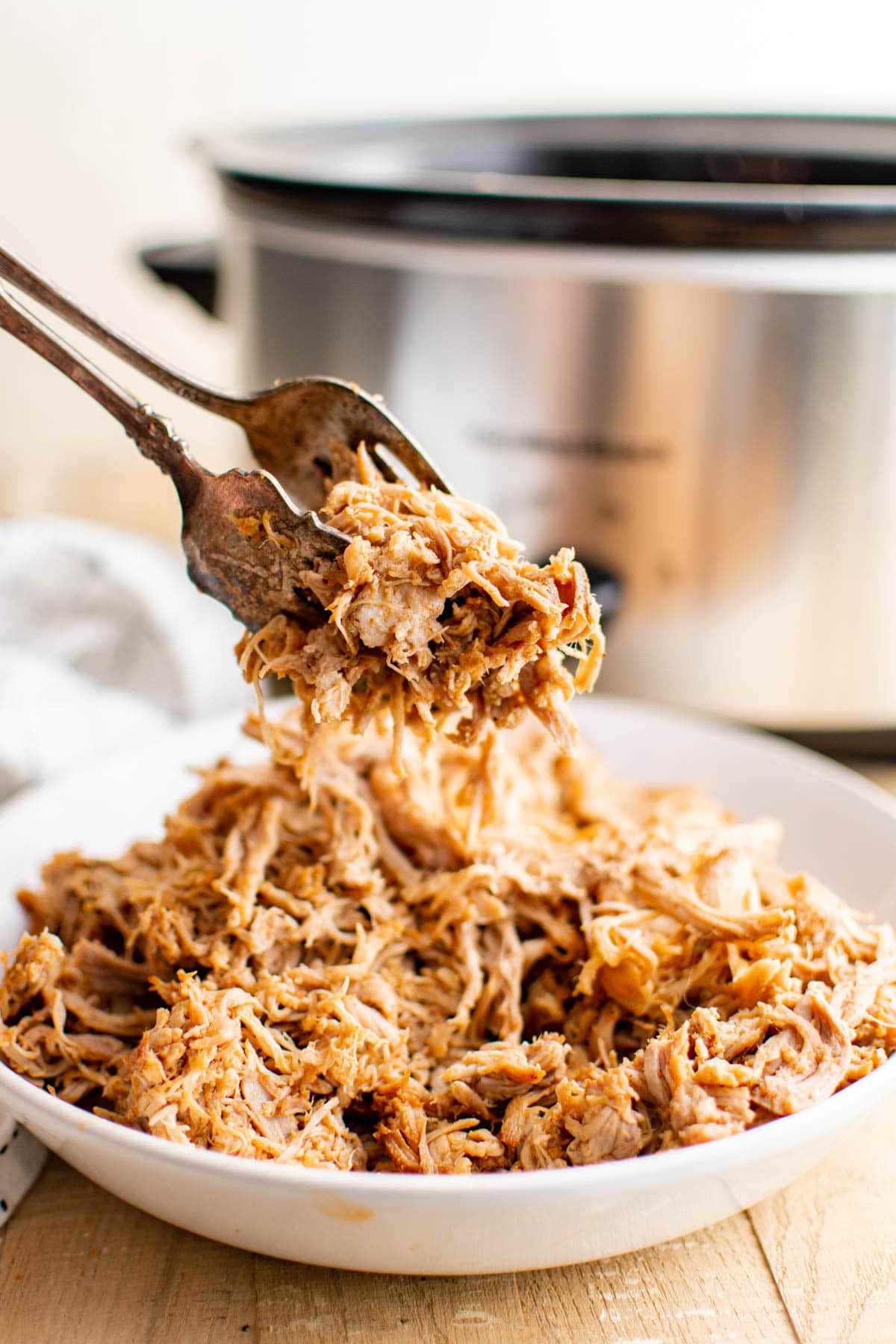 Tongs holding pulled pork oven a platter.