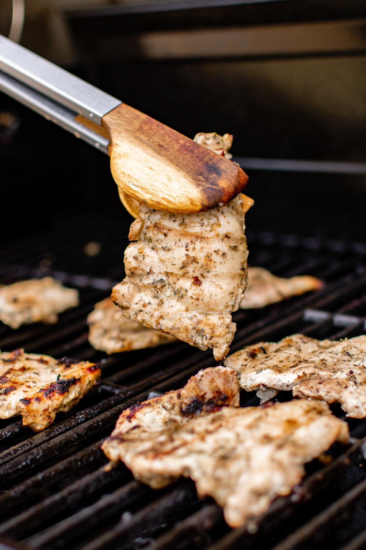 Chicken thighs grilling on a bbq with tongs. 