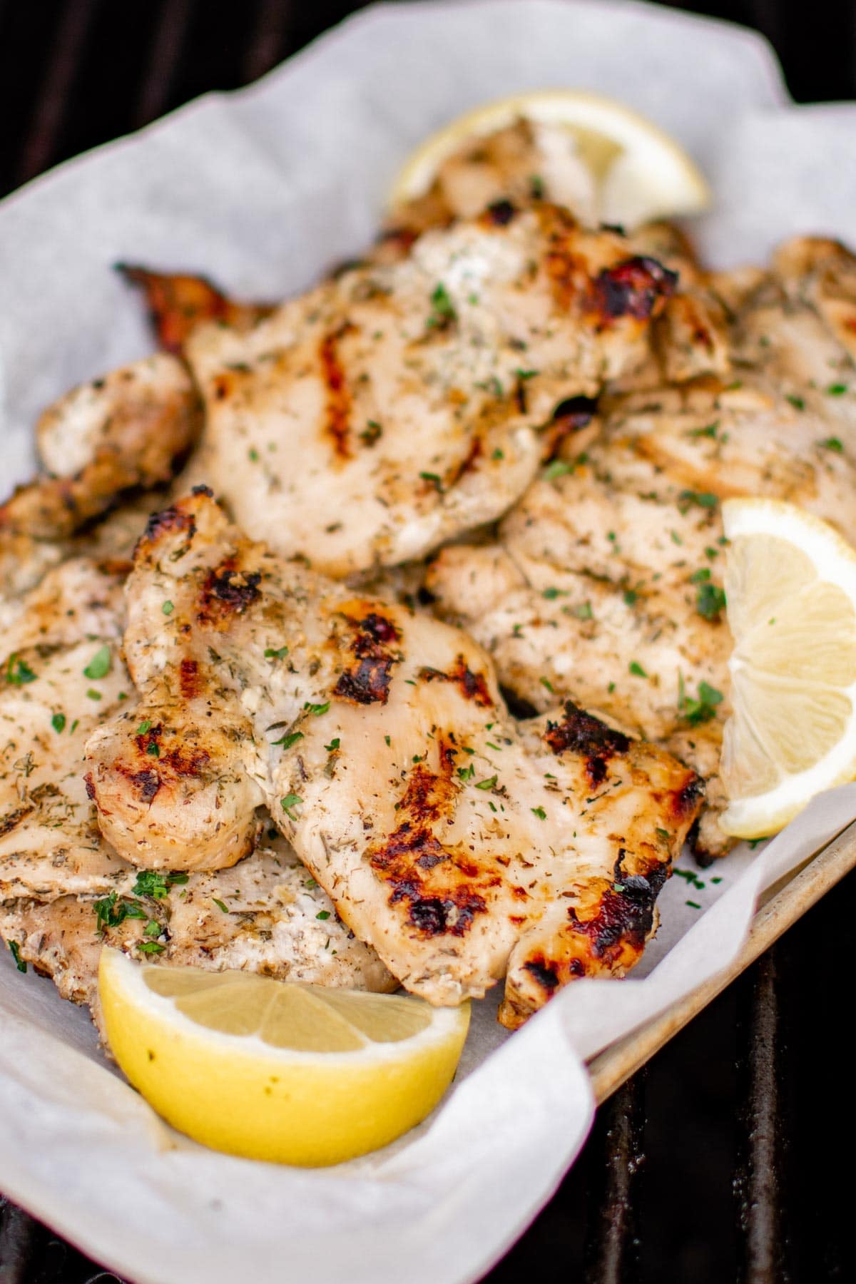 Marinated grilled chicken thighs on a white platter with lemon wedges. 