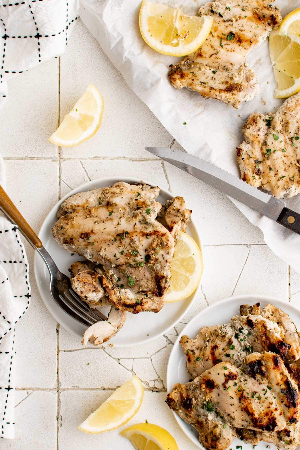 Small plates with grilled chicken, forks and lemons.