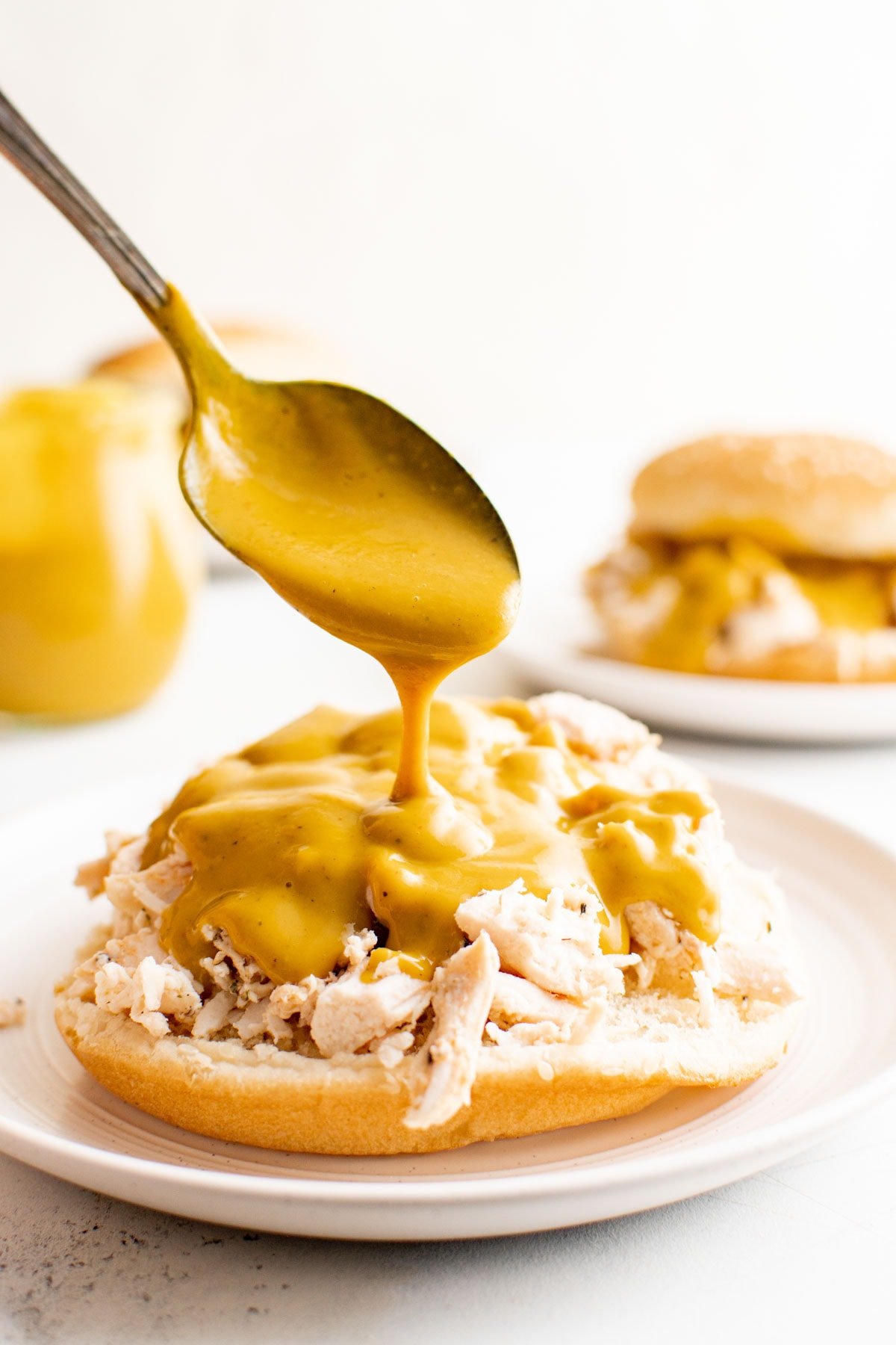 Carolina gold bbq sauce being spooned onto a shredded chicken sandwich. 