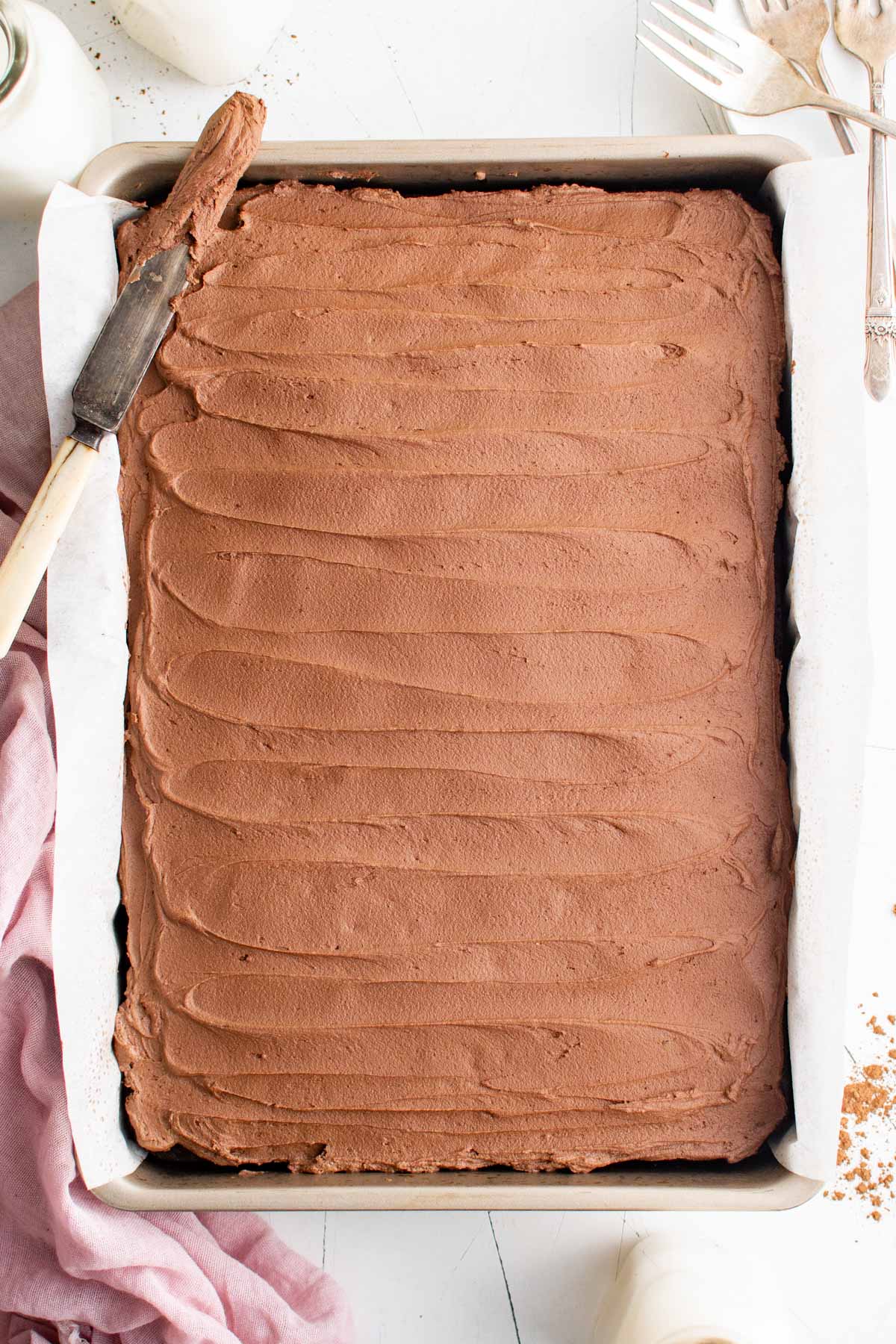Whole frosted chocolate cake in a baking pan with a knife.