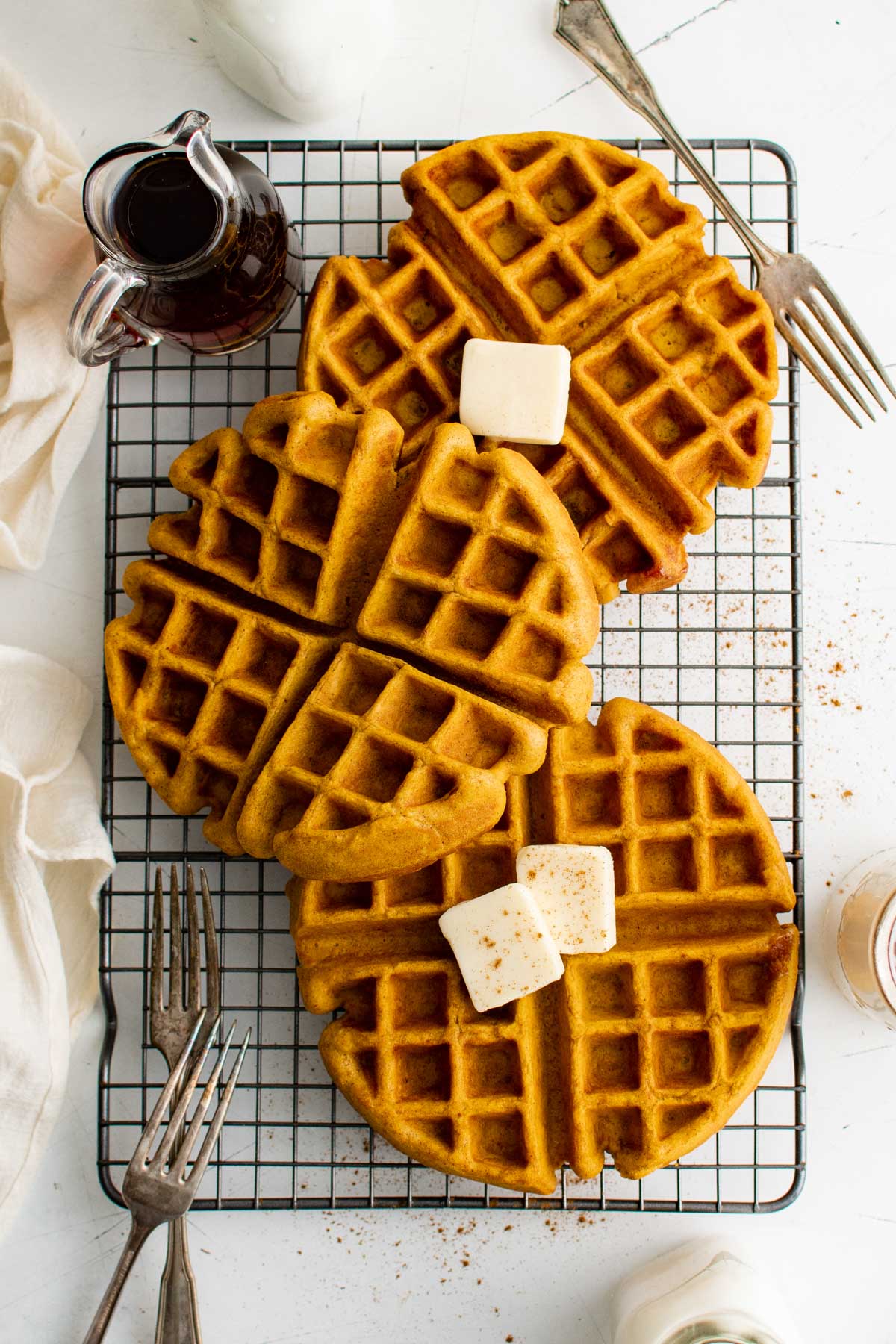 Three pumpkin waffles on a wire rack with pats of butter and a dish of syrup.