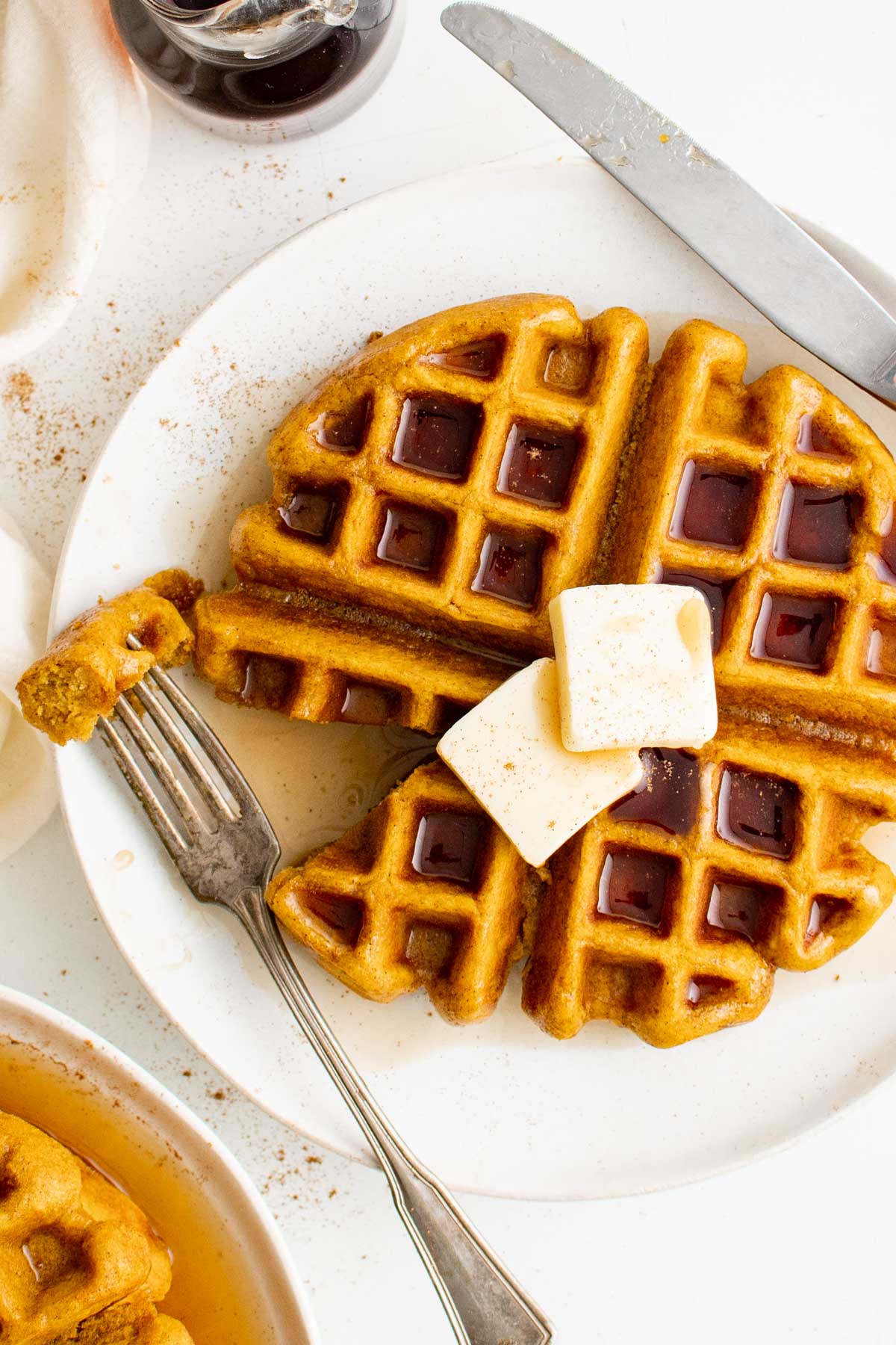 A waffle on a plate with pats of butter, cinnamon and a fork.