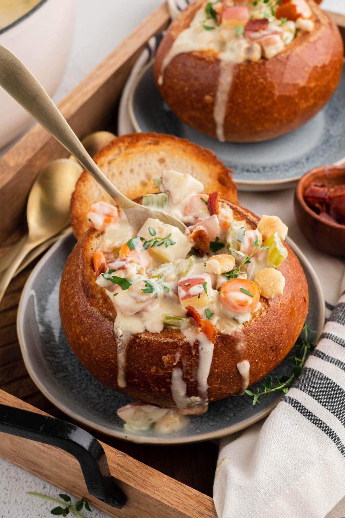 Clam chowder in a bread bowl with clam chowder dripping over the sides of the bread, with a spoon.