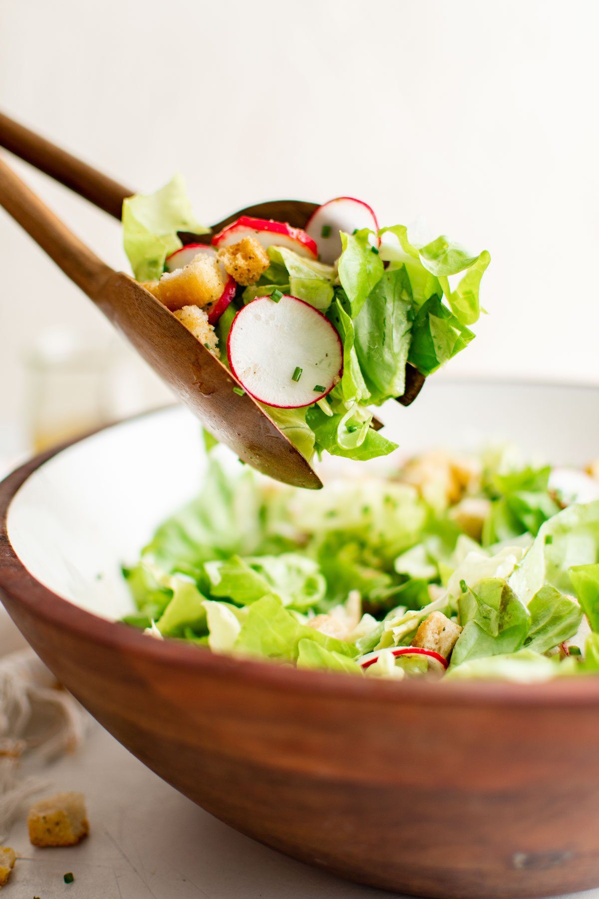 Salad serving bowl with butter lettuce, radishes and croutons, serving tongs.