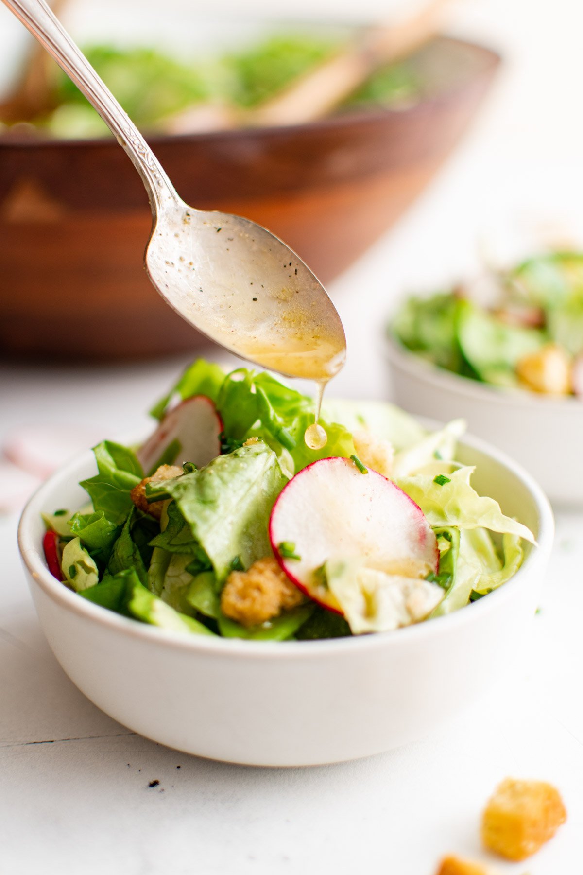 Butter lettuce salad in a white and a spoon with dressing.