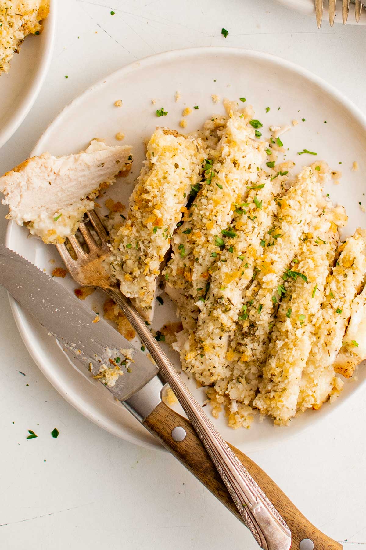 Sliced chicken breast on a white plate with breadcrumbs, a fork and knife.