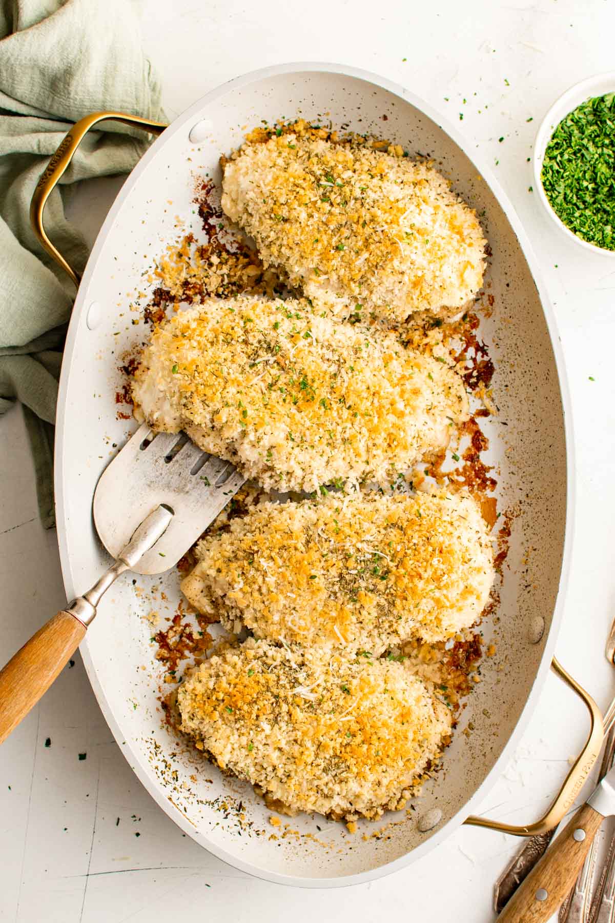 4 Chicken breasts with breadcrumbs in a white baking dish with a spatula.
