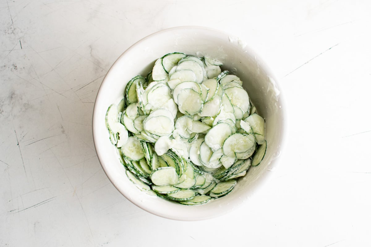 Cucumbers in a white bowl mixed with sour cream dressing.