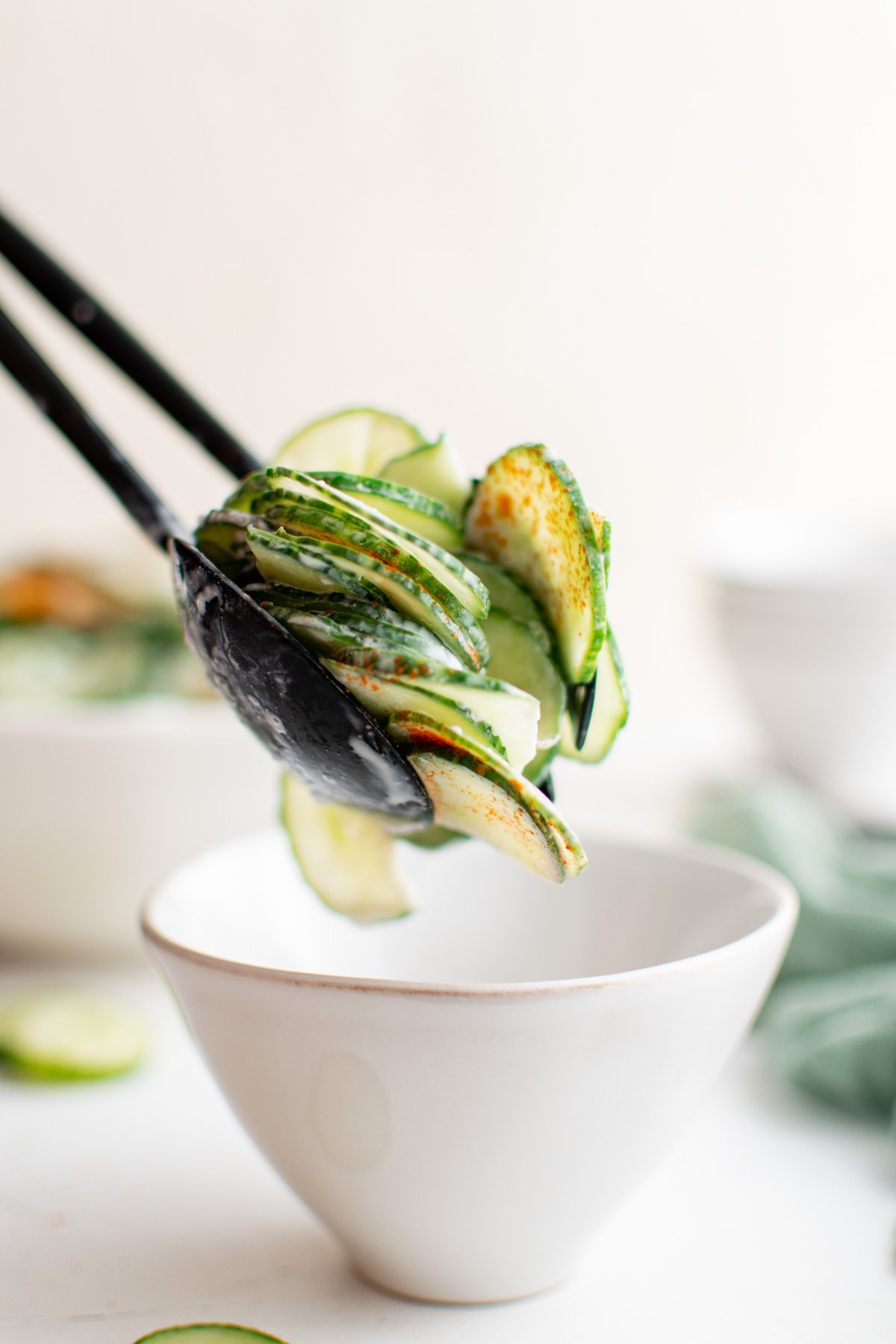 Thinly sliced cucumbers in dressing being served with salad tongs into a small white bowl.