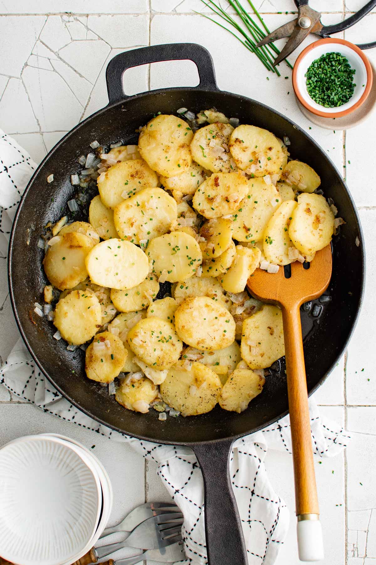 Fried potatoes in a large skillet with a wooden spatula.