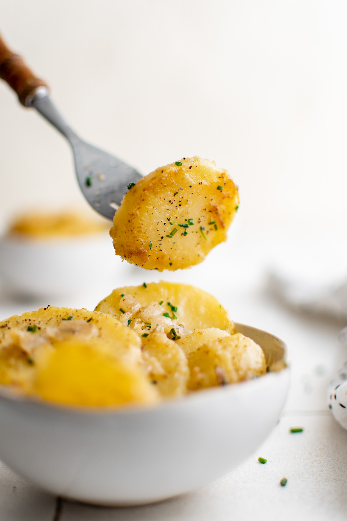 Fork with a sliced potato on it, over a small white bowl with potatoes.