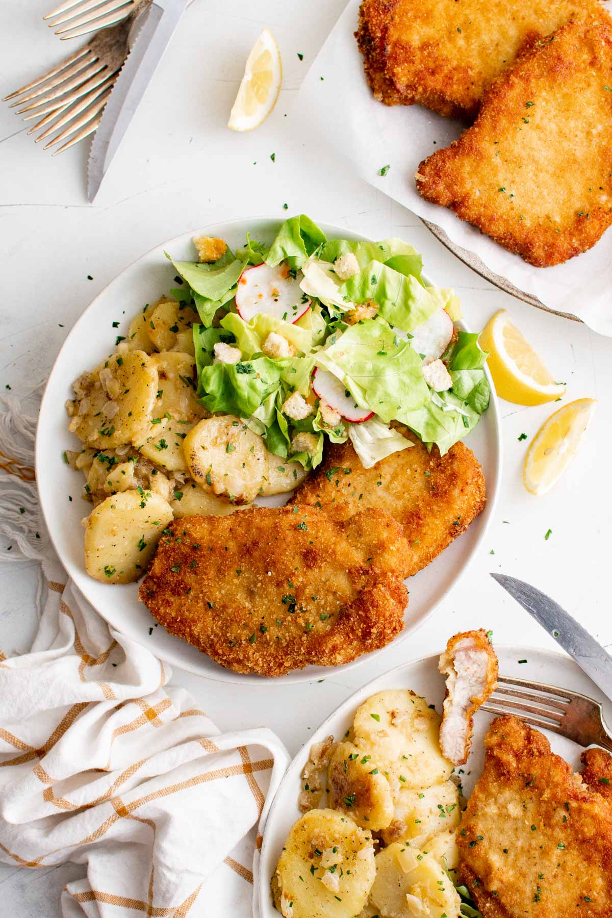 Pork Schnitzel, fried potatoes and salad on white plates.