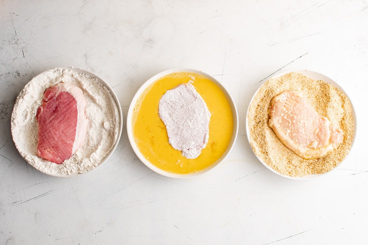 Breading stations for pork, with pork chops dipped in flour, then eggs.