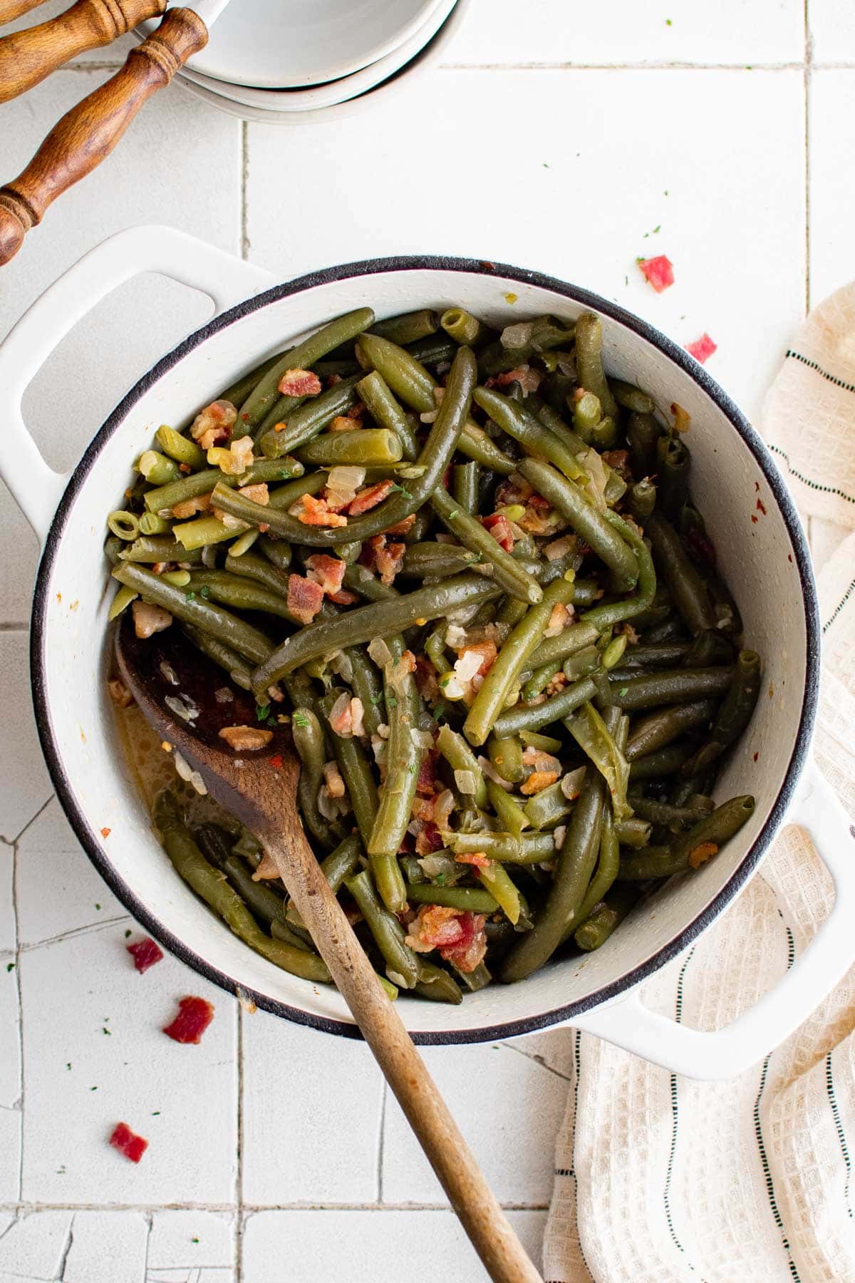 Pot with green beans and bacon and a wooden spoon.
