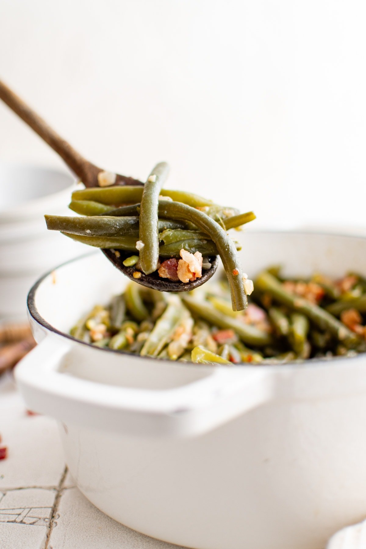 Large pot of southern green beans, a small serving lifted up by a wooden spoon.