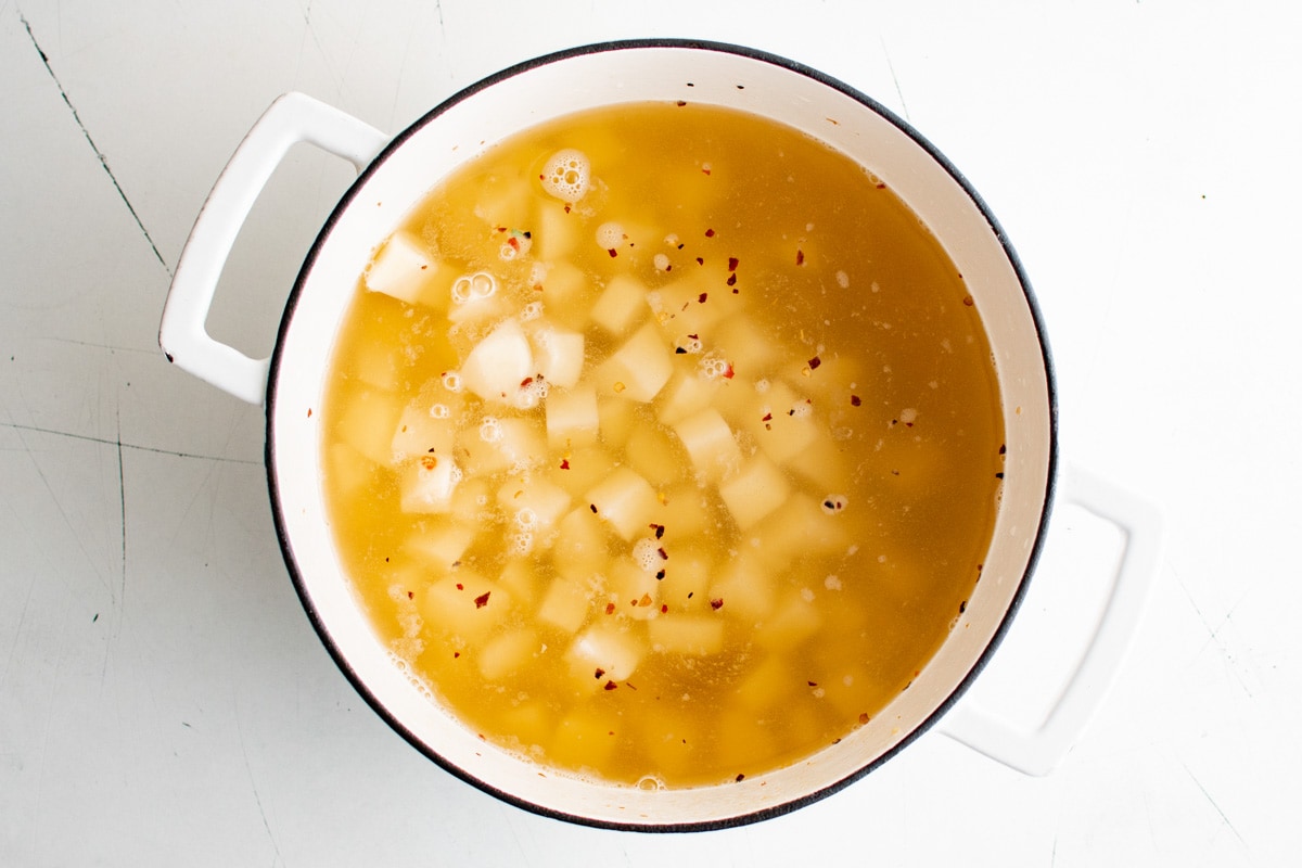 Chicken broth in a soup pot with potatoes.