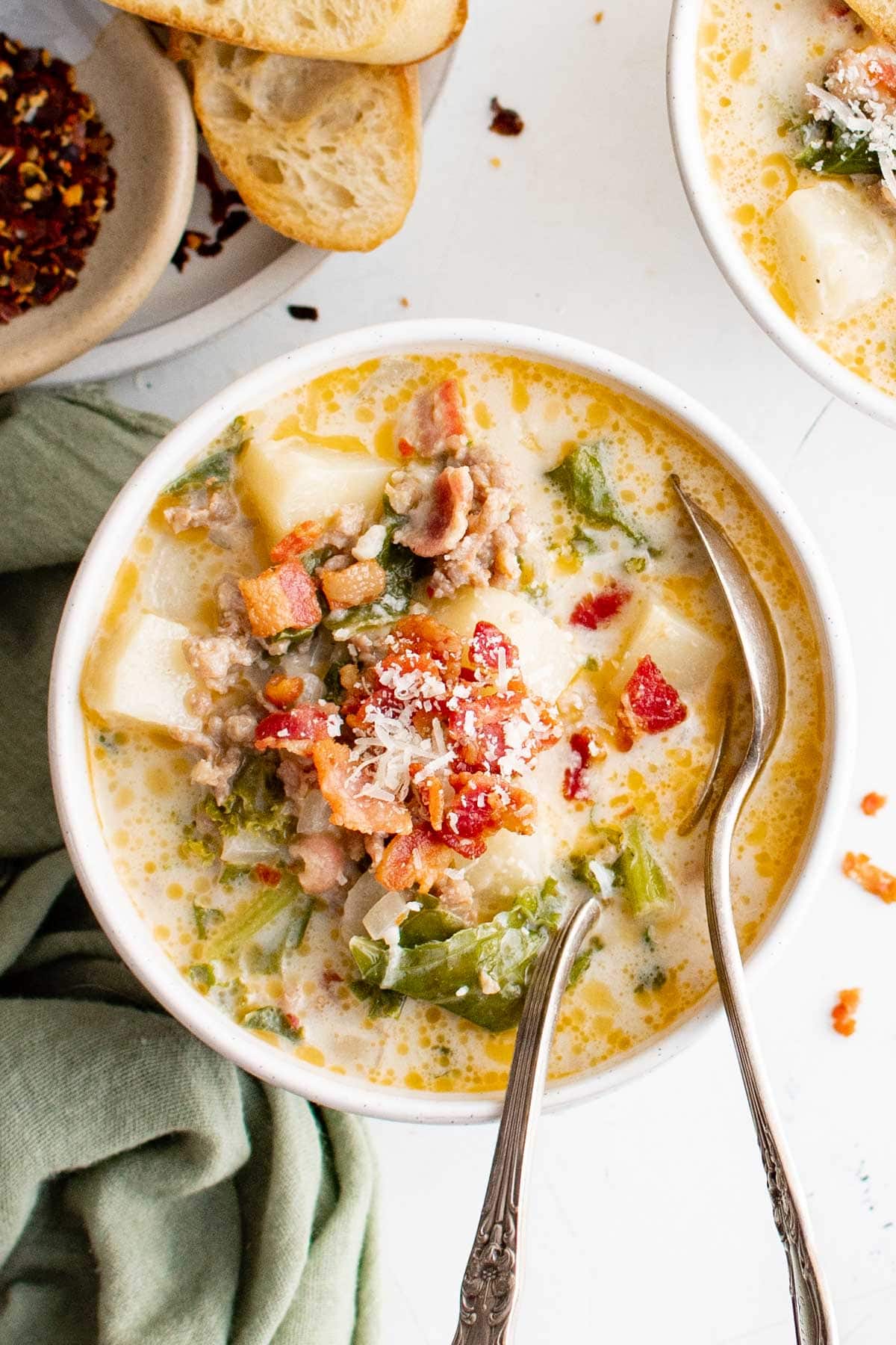 Bowl of cream based soup with sausage, bacon and kale.