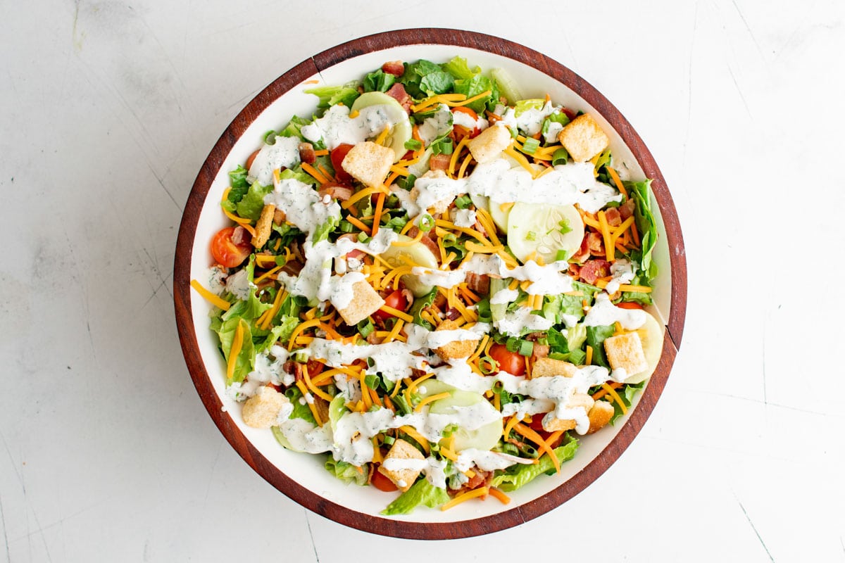 Chopped Salad in a bowl with ranch dressing, carrots, tomatoes, croutons and shredded cheese.