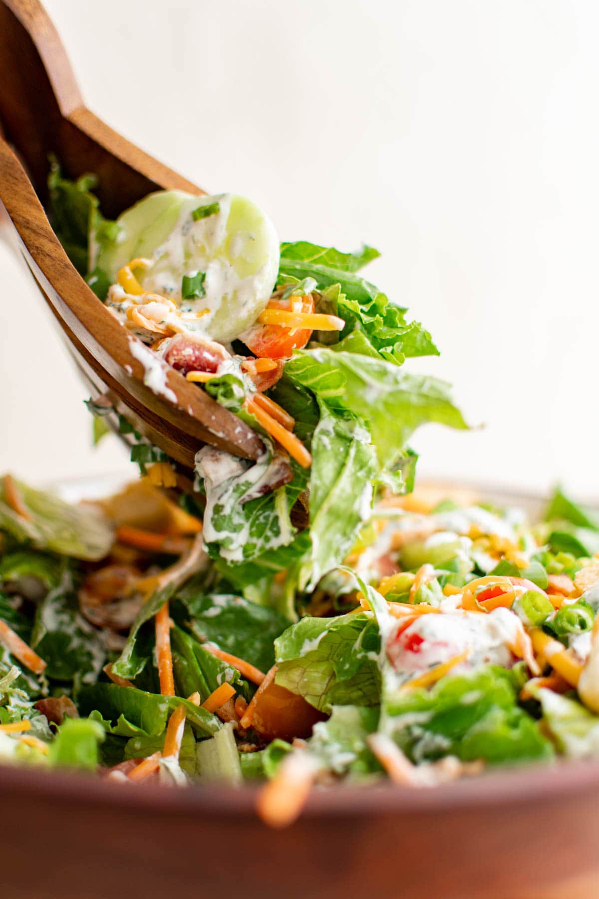 Wooden salad tongs lifting a serving of salad out of a bowl.