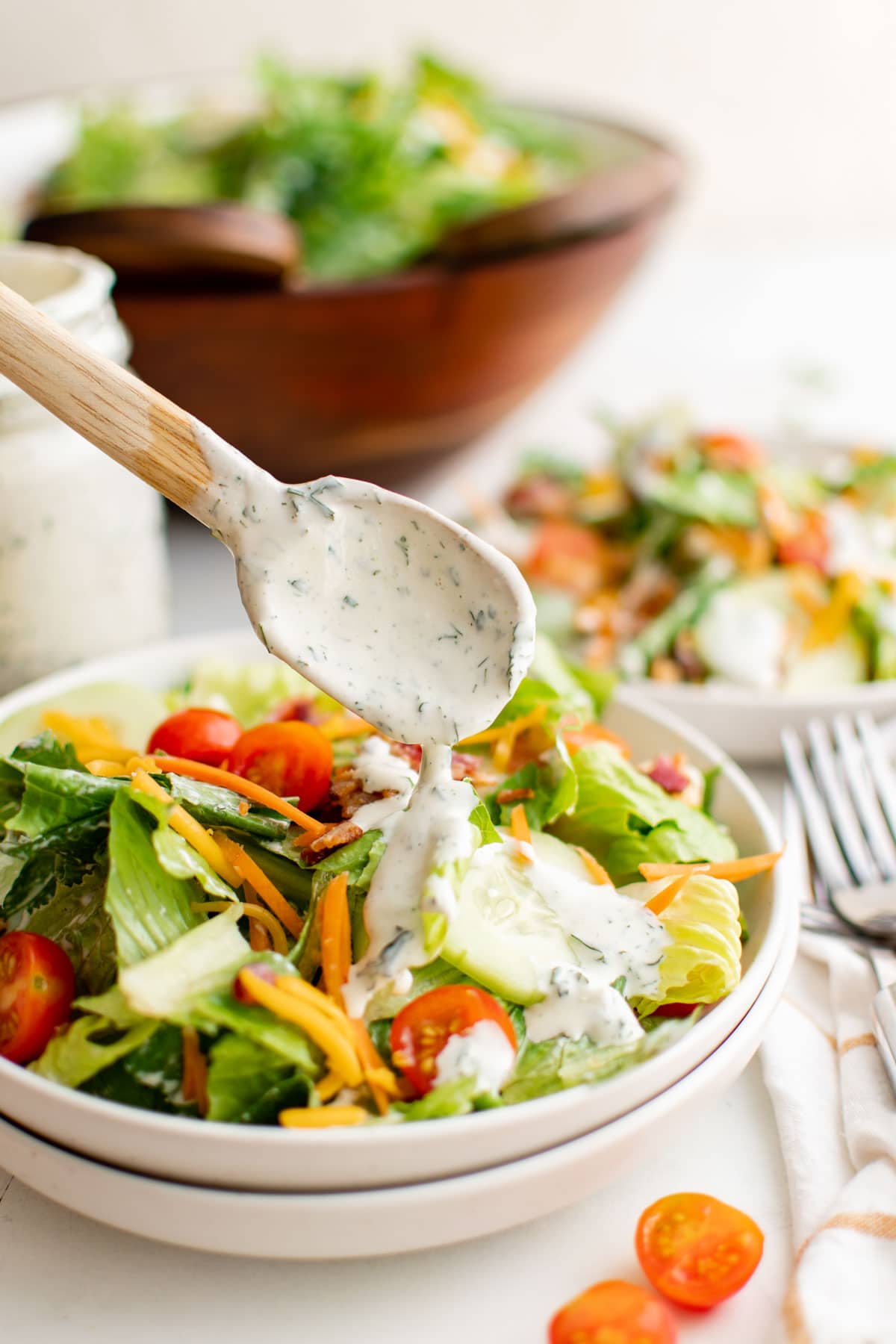 A small wooden spoon drizzling ranch dressing over a salad in a bowl.
