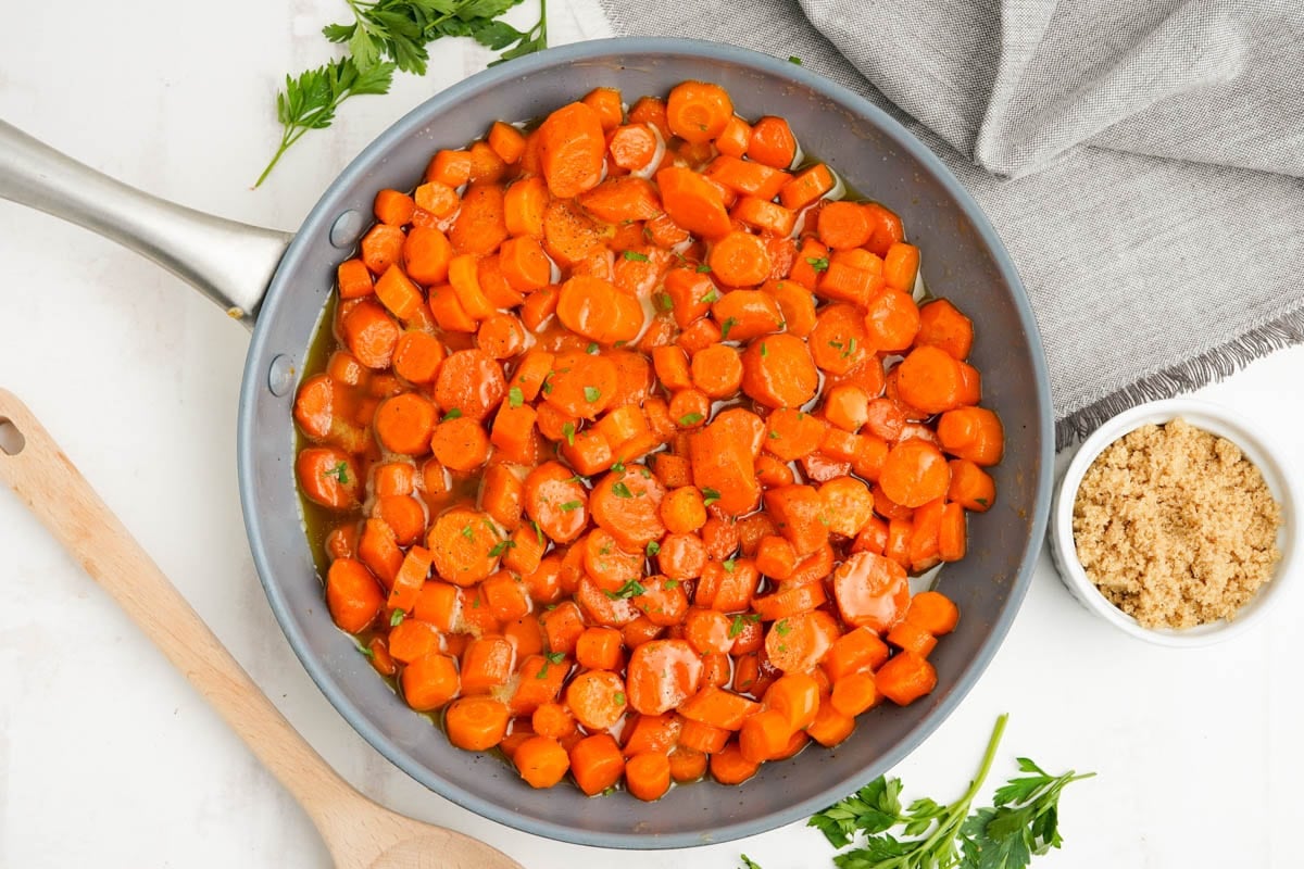 Sliced carrots tossed in brown sugar sauce in a skillet.