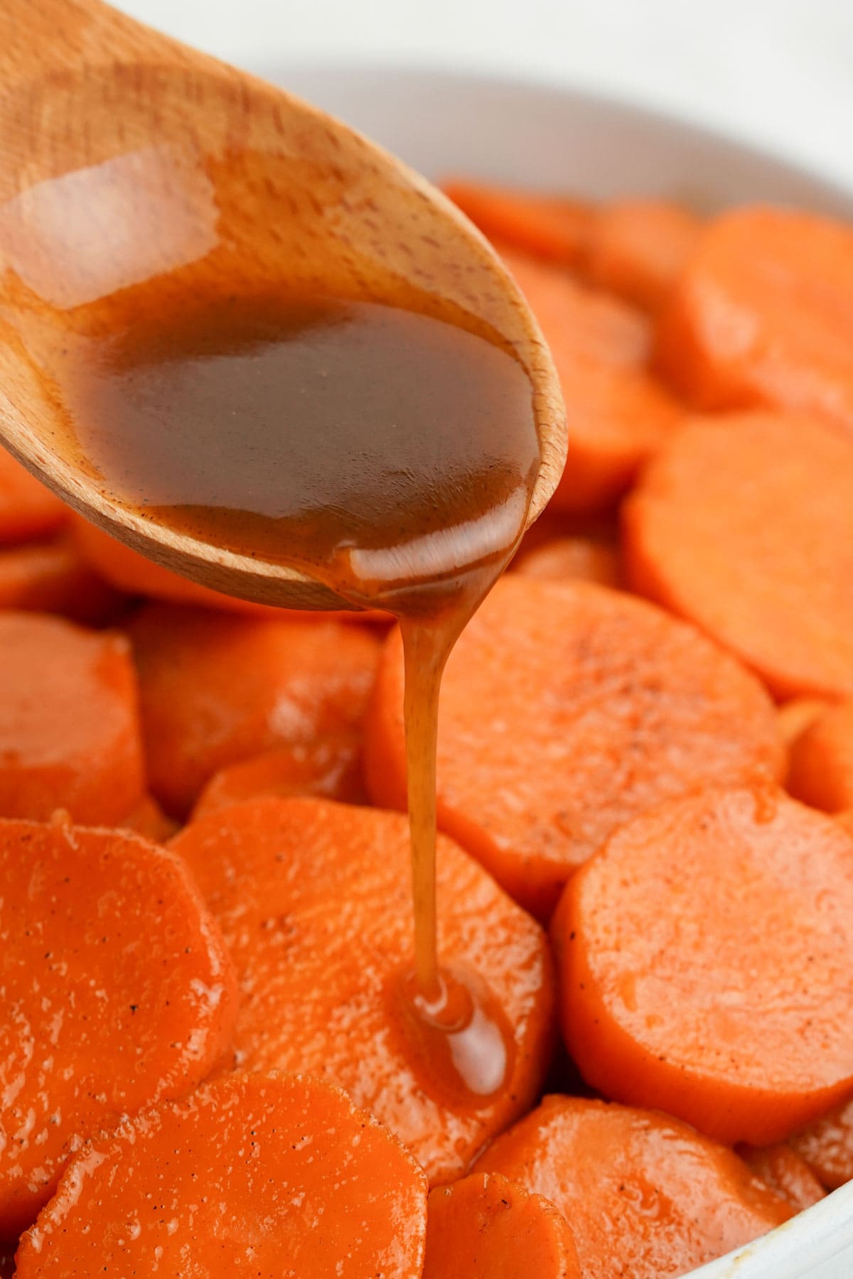 Wooden spoon with brown sugar glaze pouring over sweet potatoes.